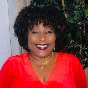 Lorna-Mae Silcott is a Black woman with short curly hair. She is wearing a bright red blouse, a diamond necklace, and a big smile.